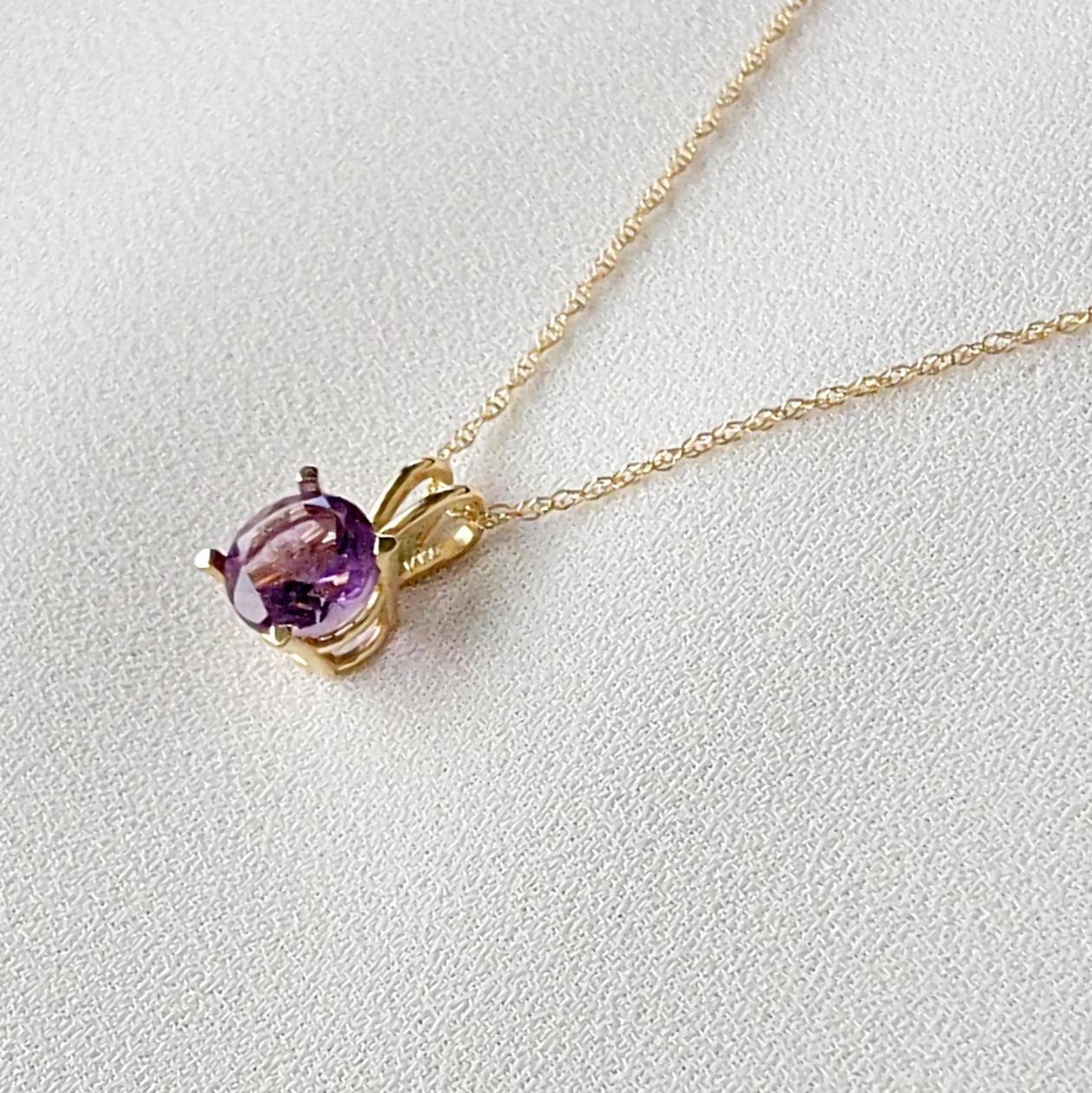 A gold chain necklace with a purple round amethyst gemstone pendant.