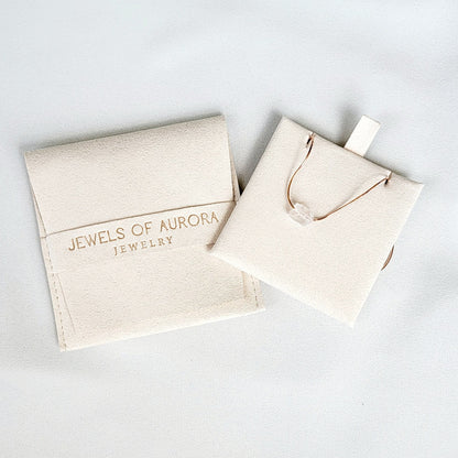 One cream velvet jewelry pouche. The larger pouch has the text &#39;Jewels of Aurora Jewelry&#39; printed on it. The smaller pouch contains a gold chain with a white crystal pendant.