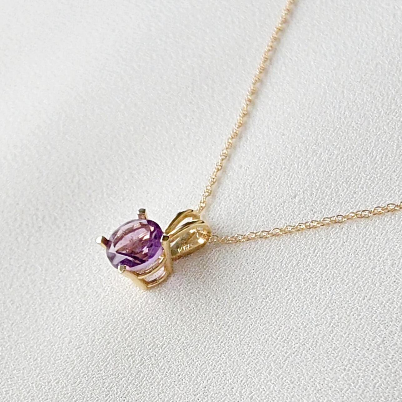 A gold chain necklace with a purple round amethyst gemstone pendant.