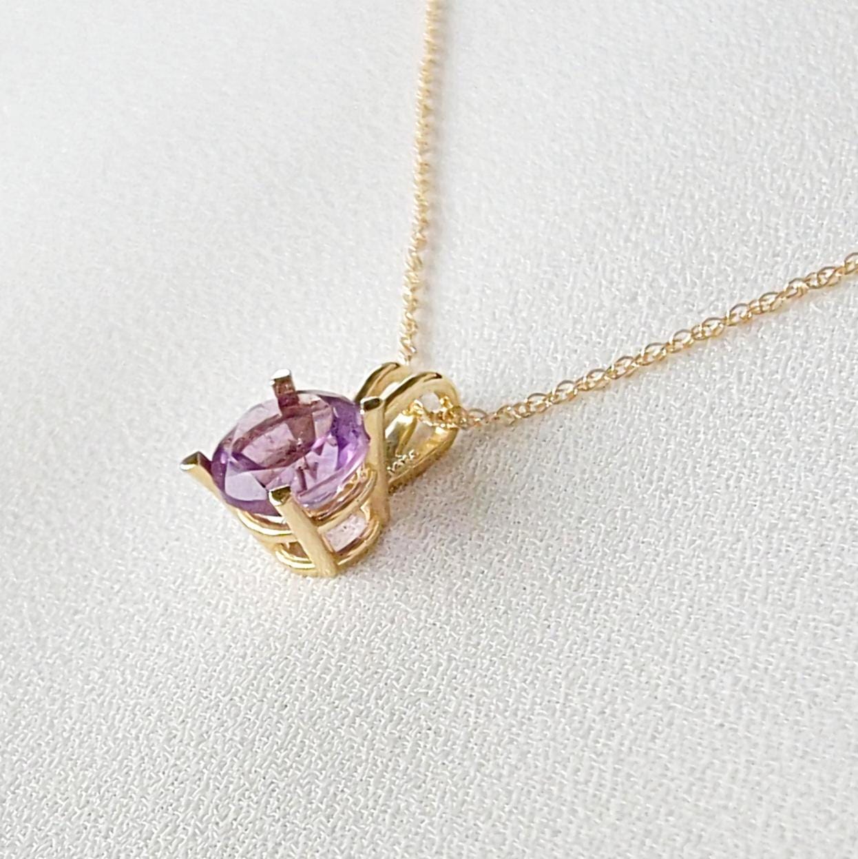 A gold chain necklace with a purple round amethyst gemstone pendant.