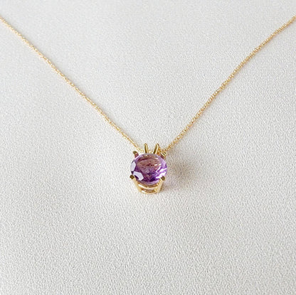 A gold chain necklace with a purple round amethyst gemstone pendant.