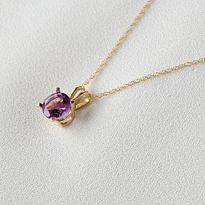 A gold chain necklace with a purple round amethyst gemstone pendant.