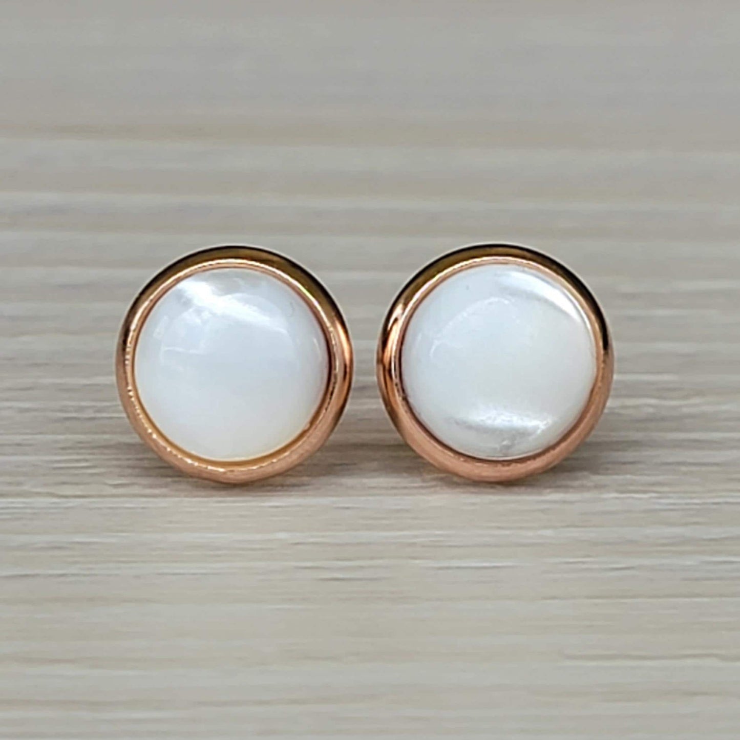 A pair of round, white mother of pearl earrings with rose gold settings.