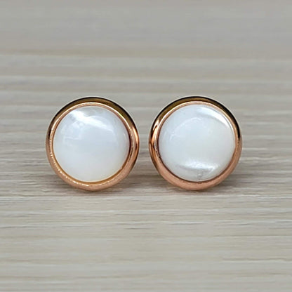A pair of round, white mother of pearl earrings with rose gold settings.