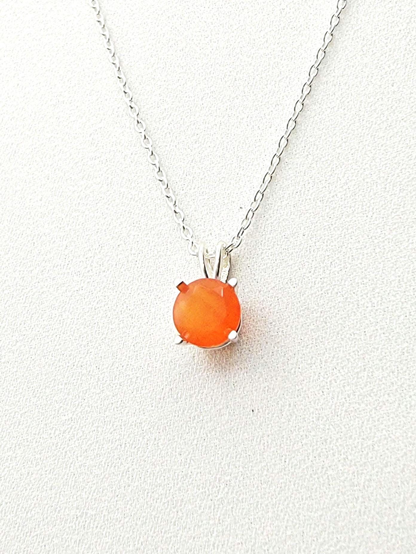 A silver necklace with a solitaire silver pendant hanging and a round faceted carnelian stone in the middle.