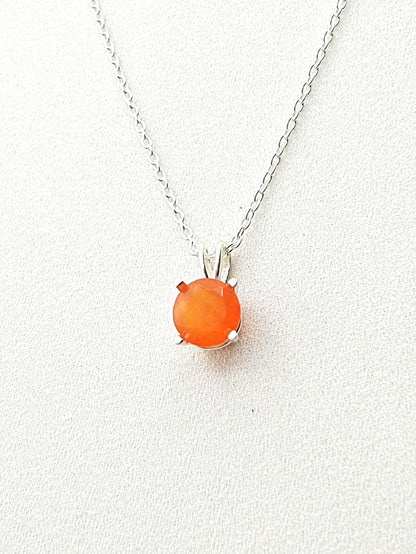 A silver necklace with a solitaire silver pendant hanging and a round faceted carnelian stone in the middle.
