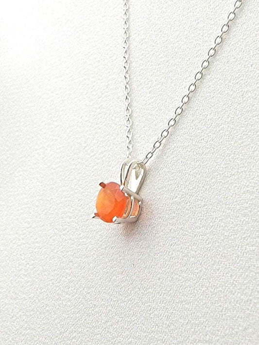 A silver necklace with a solitaire silver pendant hanging and a round faceted carnelian stone in the middle.