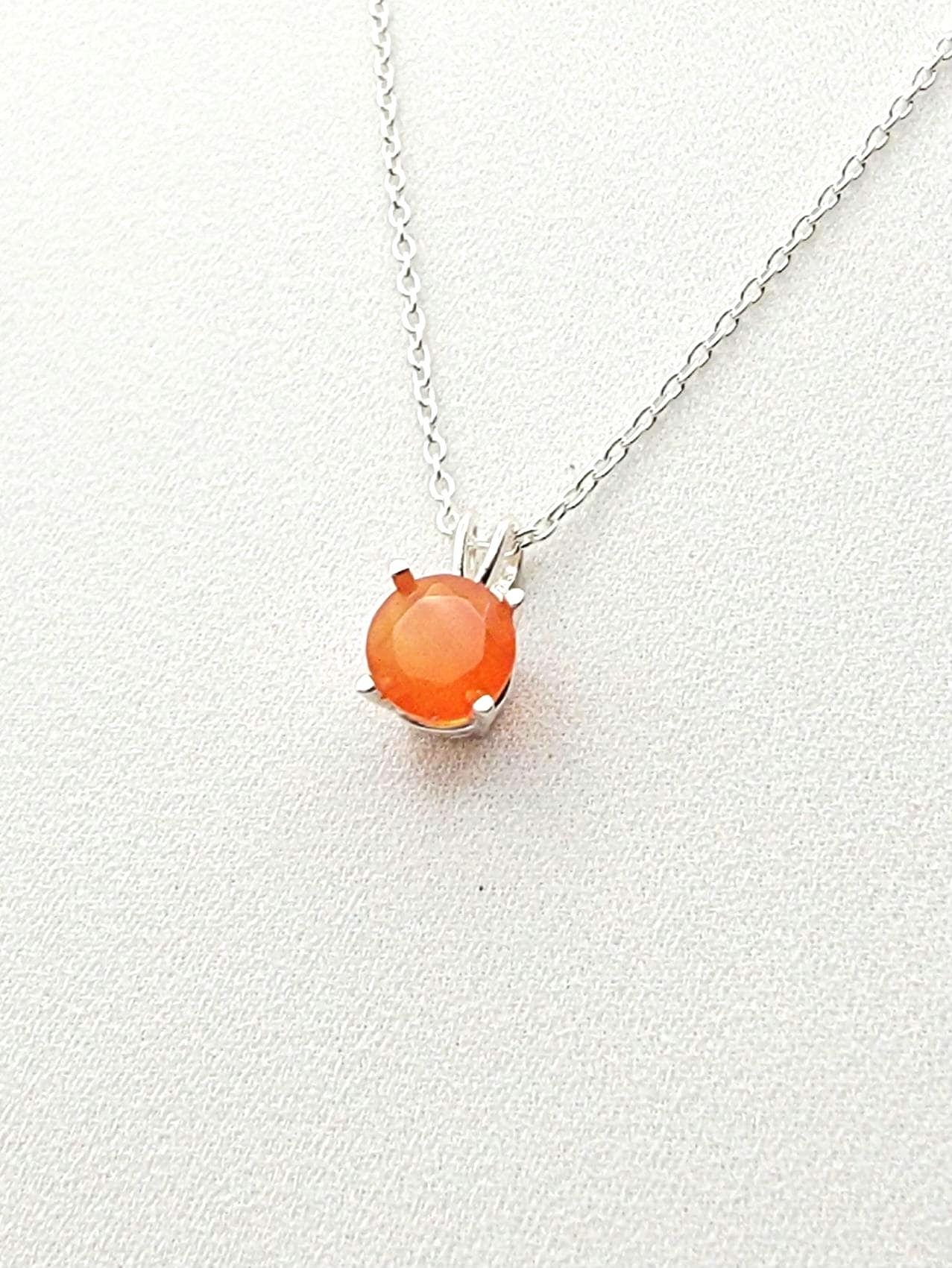 A silver necklace with a solitaire silver pendant hanging and a round faceted carnelian stone in the middle.