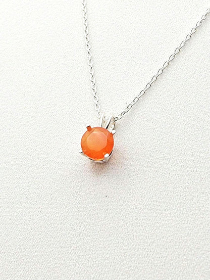 A silver necklace with a solitaire silver pendant hanging and a round faceted carnelian stone in the middle.