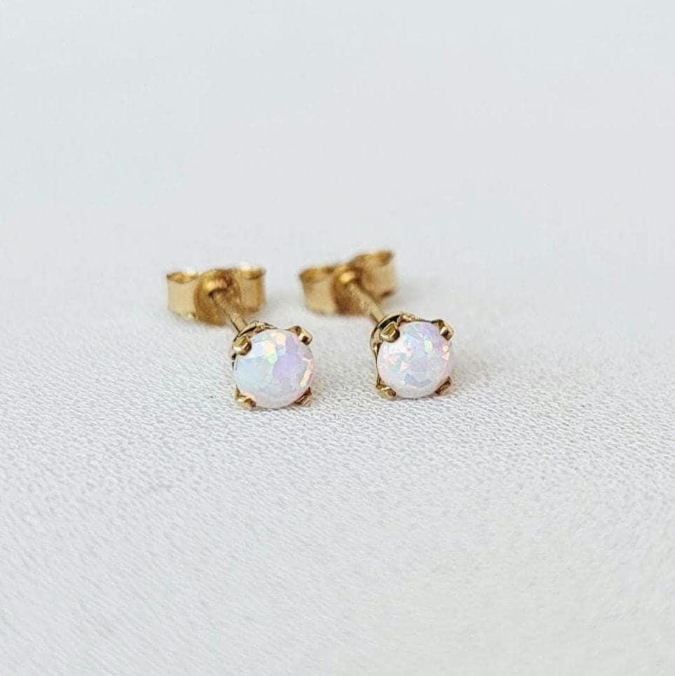 A pair of gold stud earrings with white opalite gemstones. The earrings are small and delicate, and the opalites have a subtle iridescent shimmer.