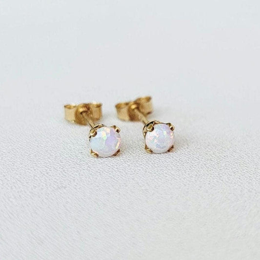 A pair of gold stud earrings with white opalite gemstones. The earrings are small and delicate, and the opalites have a subtle iridescent shimmer.