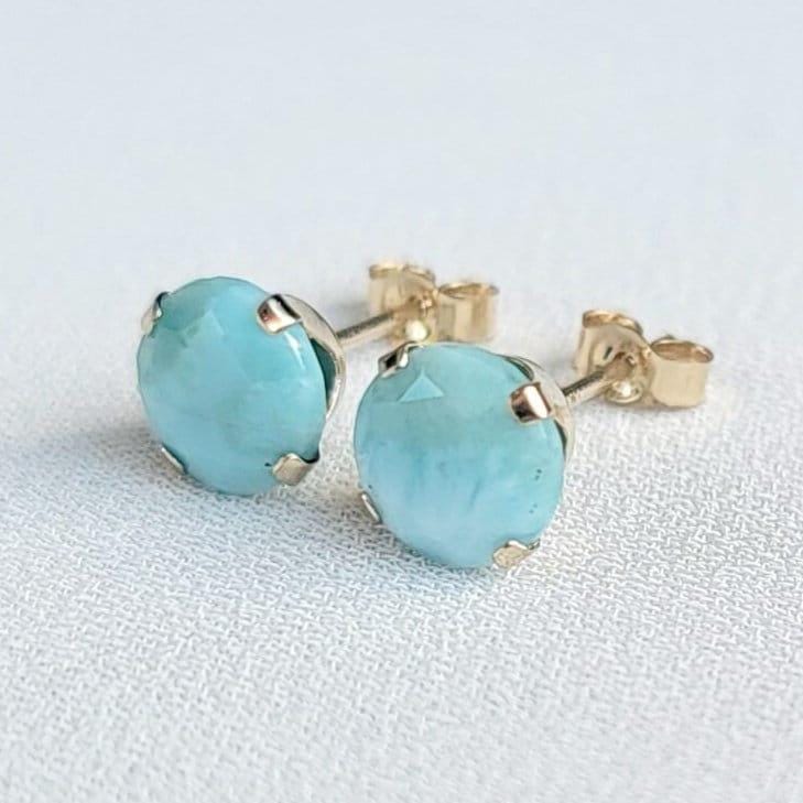 A pair of gold stud earrings with faceted round blue larimar gemstones.
