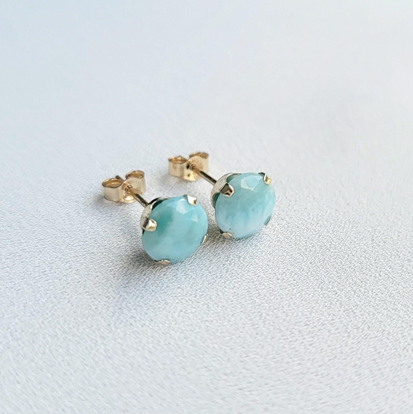 A pair of gold stud earrings with faceted round blue larimar gemstones.