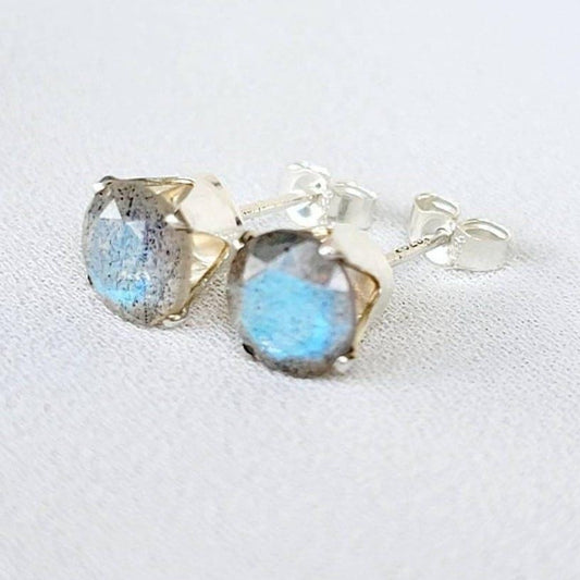 A pair of silver stud earrings with round-shaped blue labradorite gemstones. The earrings have a simple design with a smooth silver setting.
