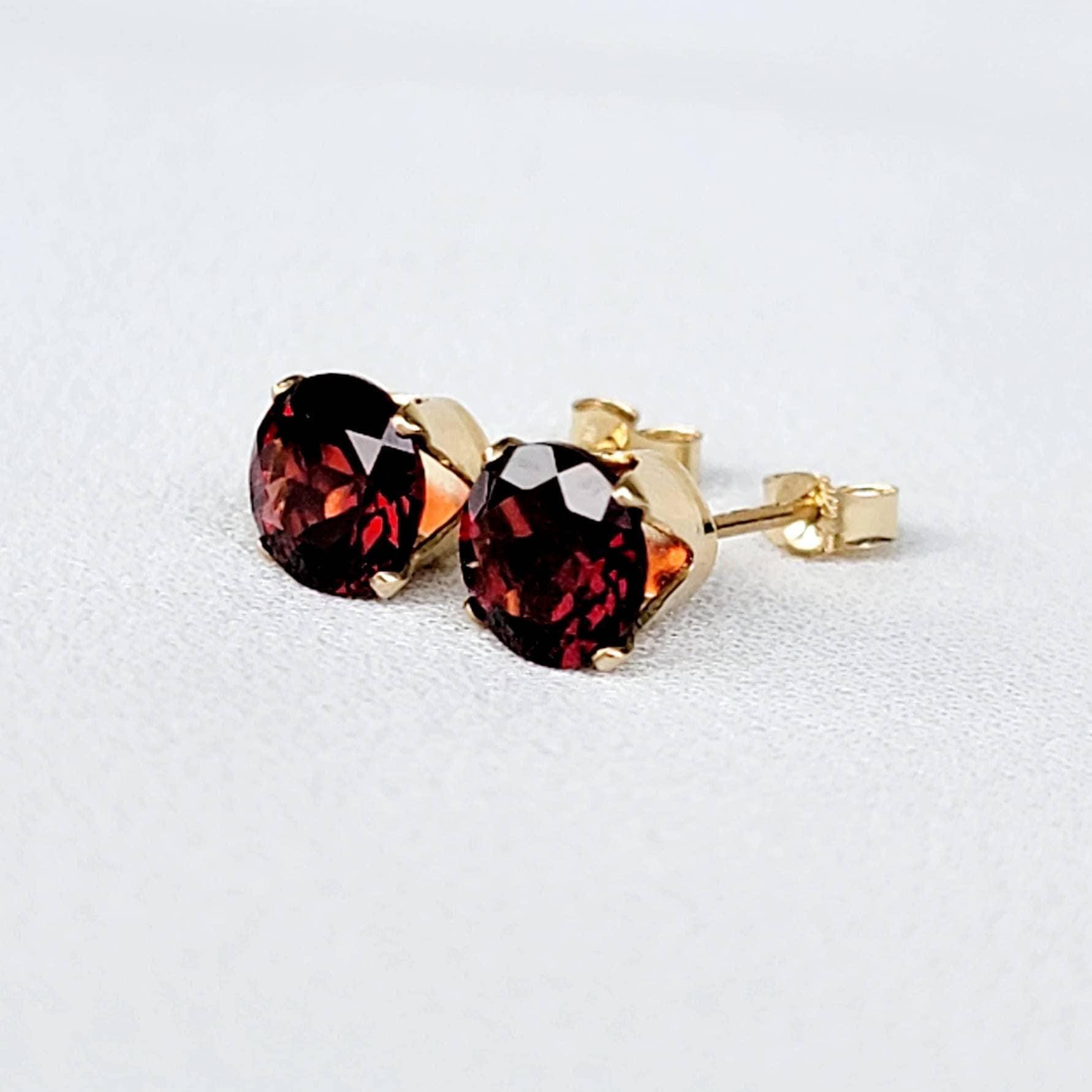 A pair of gold stud earrings with red gemstones. The gemstones are round and have a faceted cut.