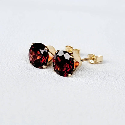 A pair of gold stud earrings with red gemstones. The gemstones are round and have a faceted cut.
