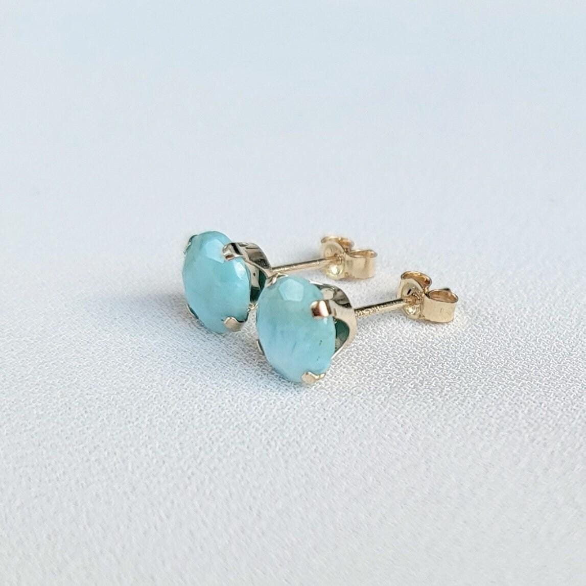 A pair of gold stud earrings with faceted round blue larimar gemstones.