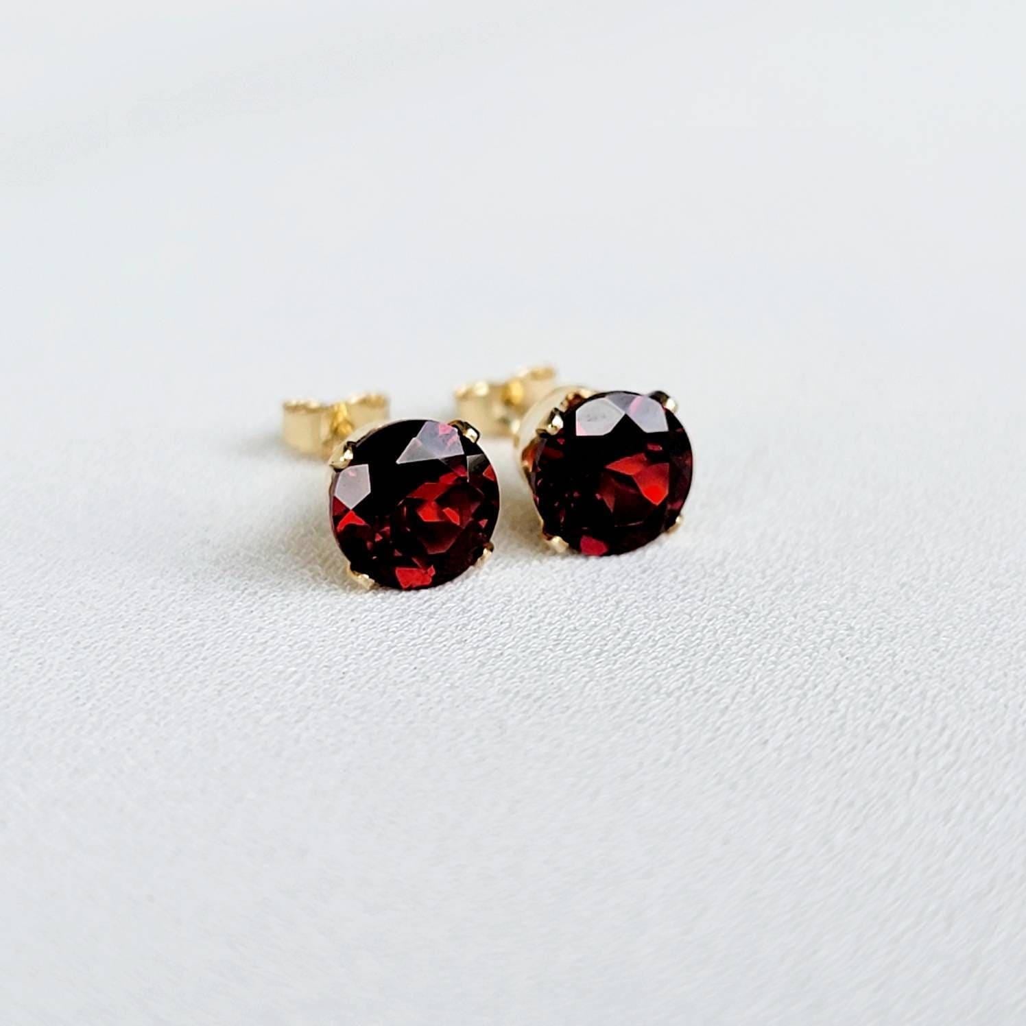 A pair of gold earrings with round, red gemstones. The earrings are on a white background.