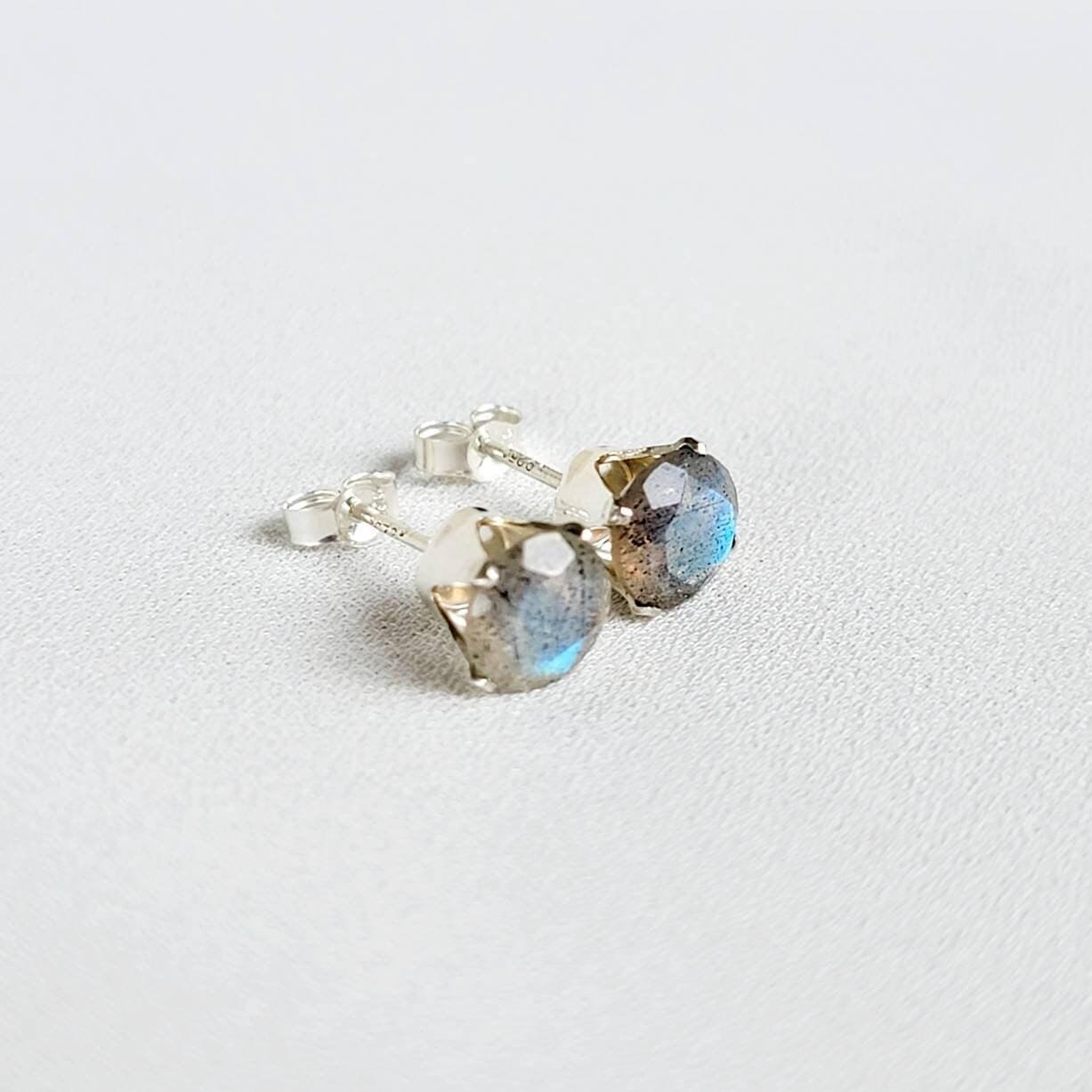 A pair of silver stud earrings with round, iridescent blue and gray labradorite gemstones.