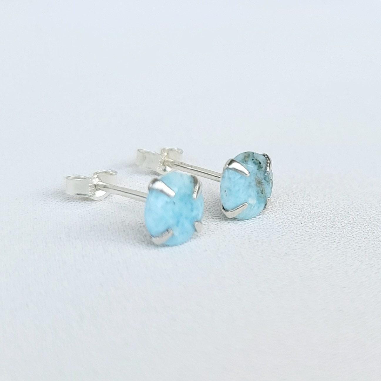 A pair of silver stud earrings with light blue Larimar round gemstones. The gemstones have a speckled pattern.