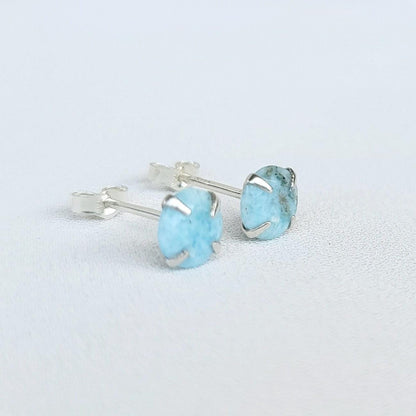 A pair of silver stud earrings with light blue Larimar round gemstones. The gemstones have a speckled pattern.