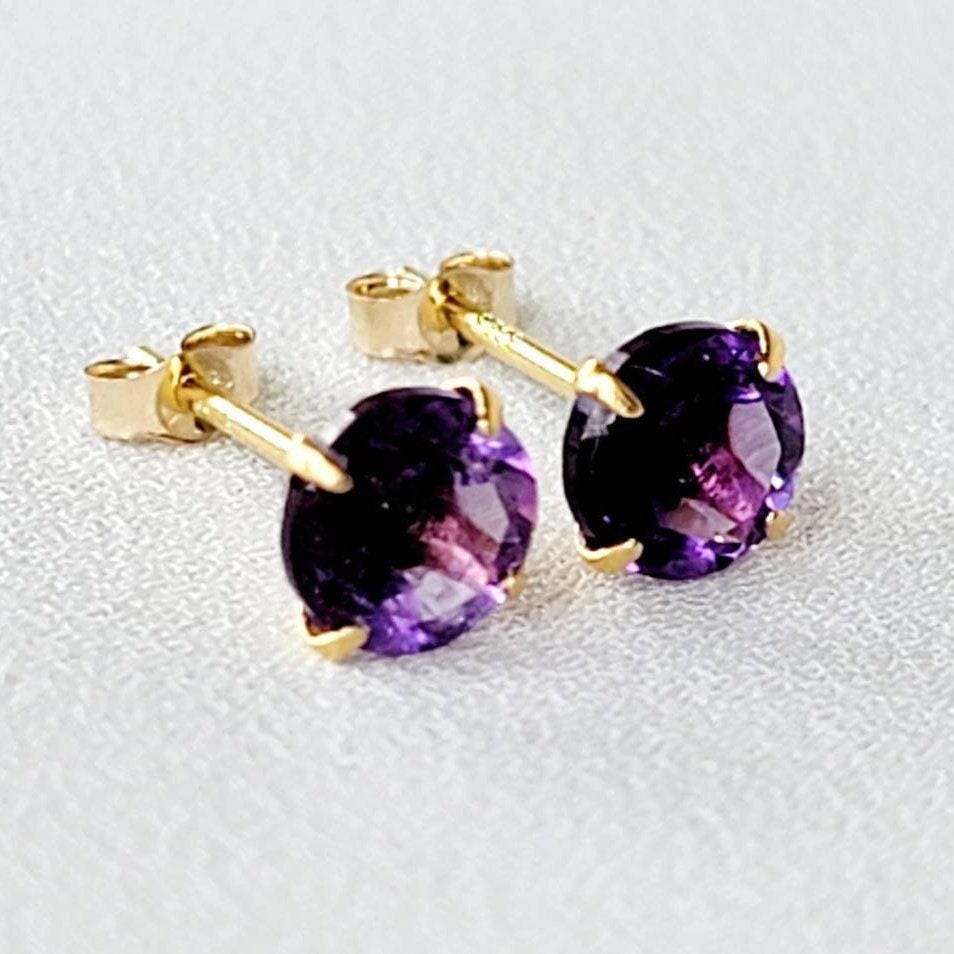 A pair of gold stud earrings with round purple amethyst gemstones.