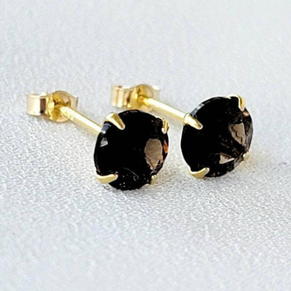 May include: A pair of gold stud earrings with round, dark brown smoky quartz gemstones.