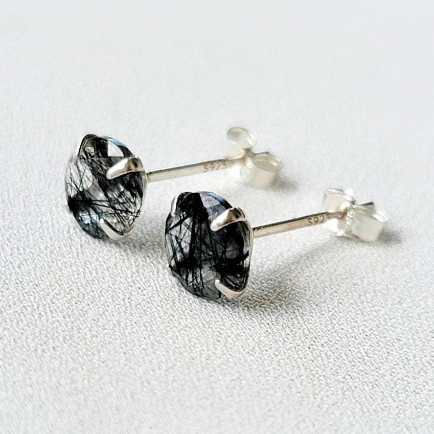 A pair of silver stud earrings with black spikes going through clear quartz. The earrings are marked with &#39;S925&#39; on the posts.