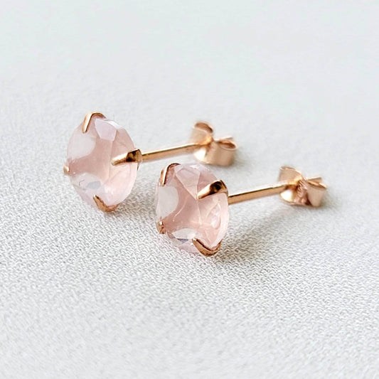 Rose gold stud earrings featuring round faceted rose quartz gemstones. Each earring showcases a light pink, translucent stone securely set in a four-prong rose gold setting. The posts and butterfly backs are also crafted from rose gold, ensuring a cohesive and elegant look. These delicate earrings are perfect for adding a touch of understated glamour to any outfit.