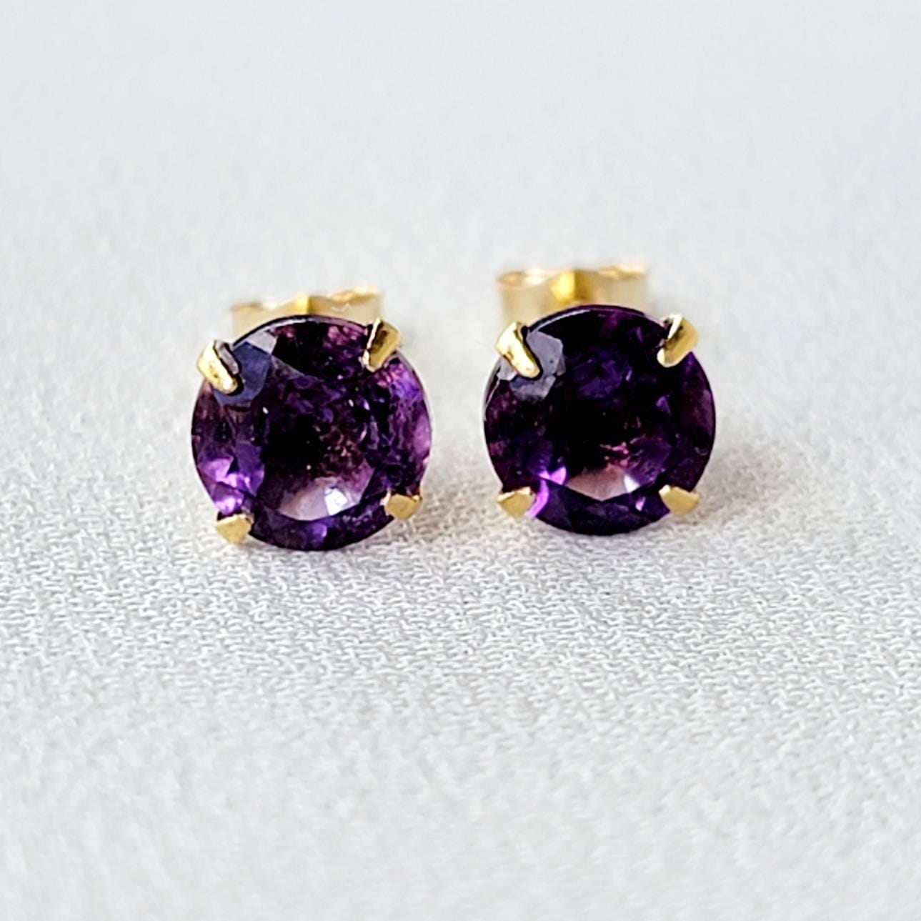 A pair of gold stud earrings with round, purple amethyst gemstones