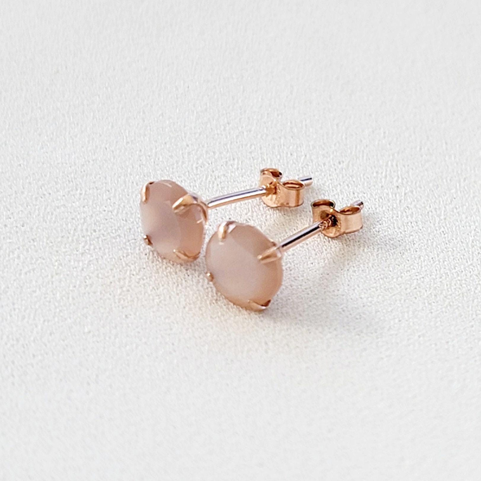 A pair of rose gold stud earrings with round, light peachy pink stones set in a prong setting.