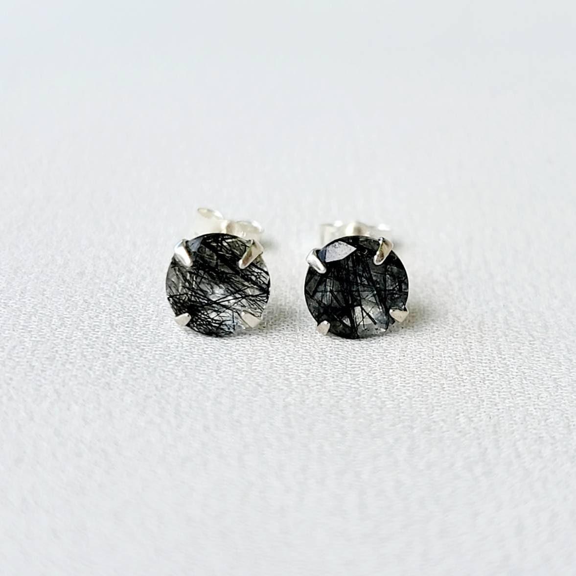 A pair of silver stud earrings with black spikes going through clear quartz. The earrings are marked with &#39;S925&#39; on the posts.