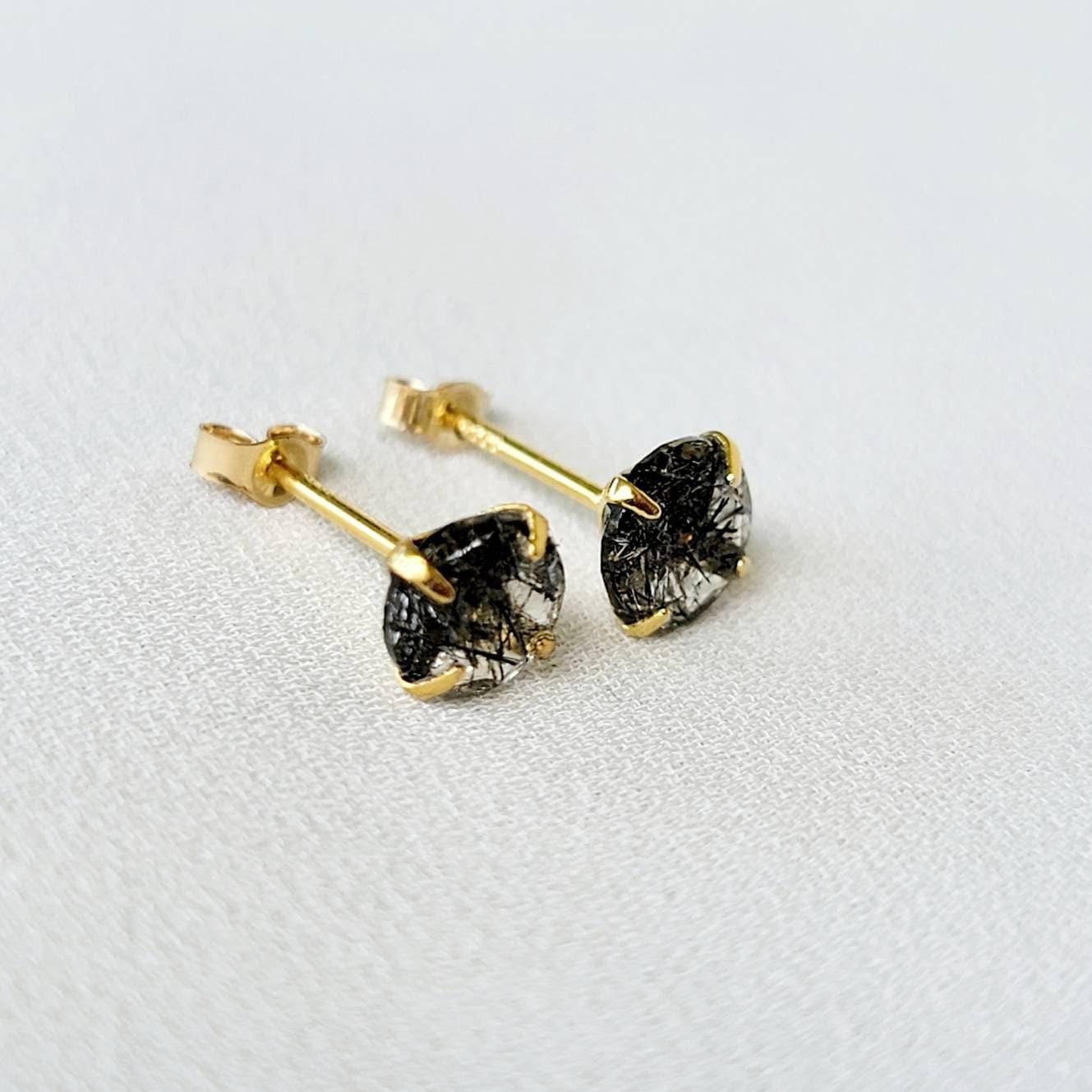 A pair of gold stud earrings with black spikes going through clear quartz. The earrings are marked with &#39;S925&#39; on the posts.