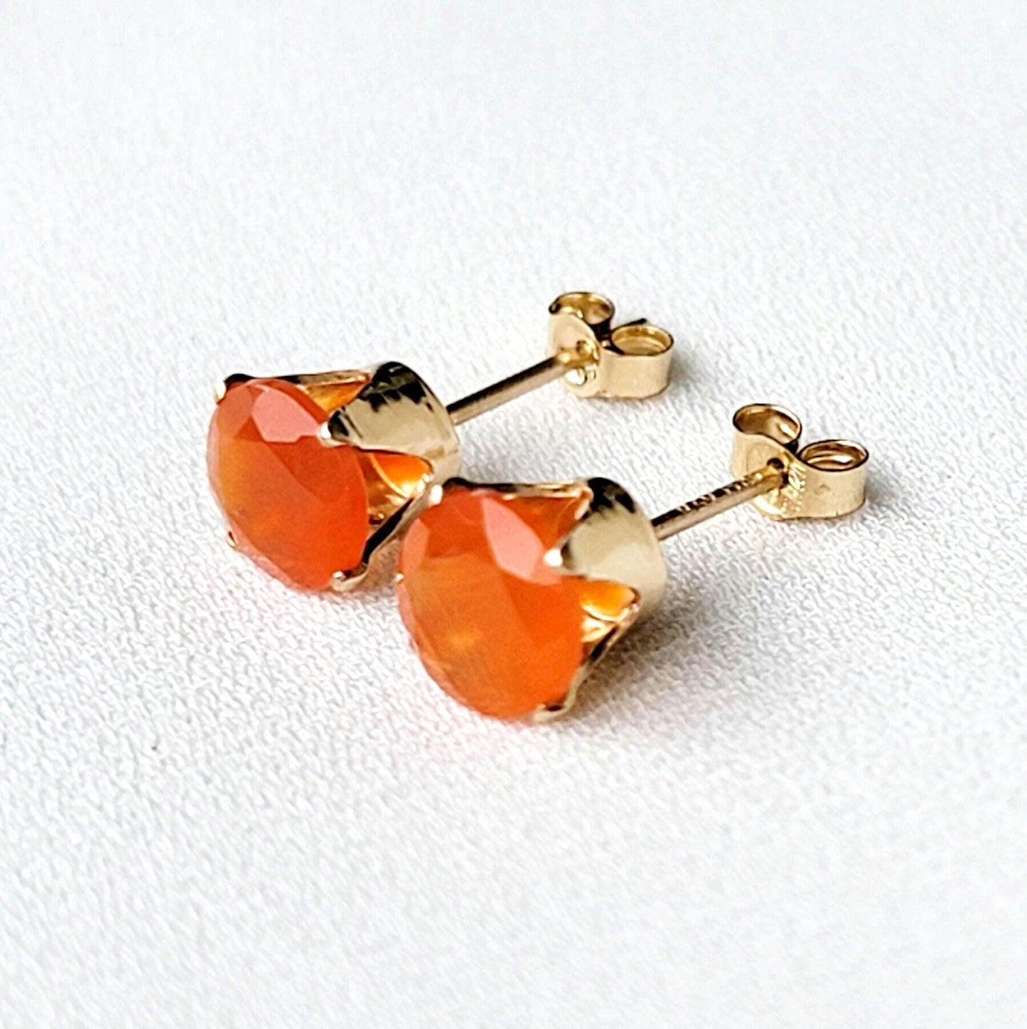 A pair of gold stud earrings with orange carnelian gemstones. The earrings have a simple design with a round gemstone set in a gold setting.