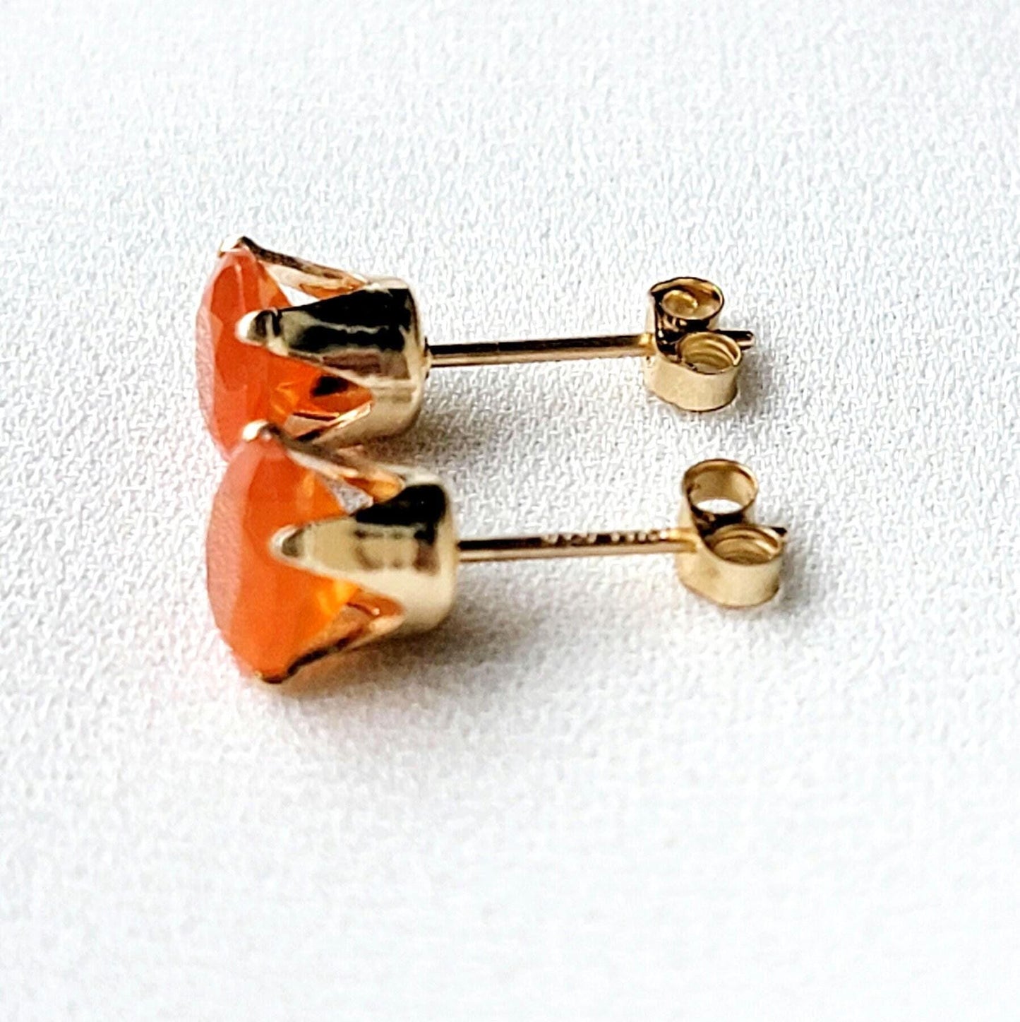 A pair of gold stud earrings with orange carnelian gemstones. The earrings have a simple design with a round gemstone set in a gold setting.