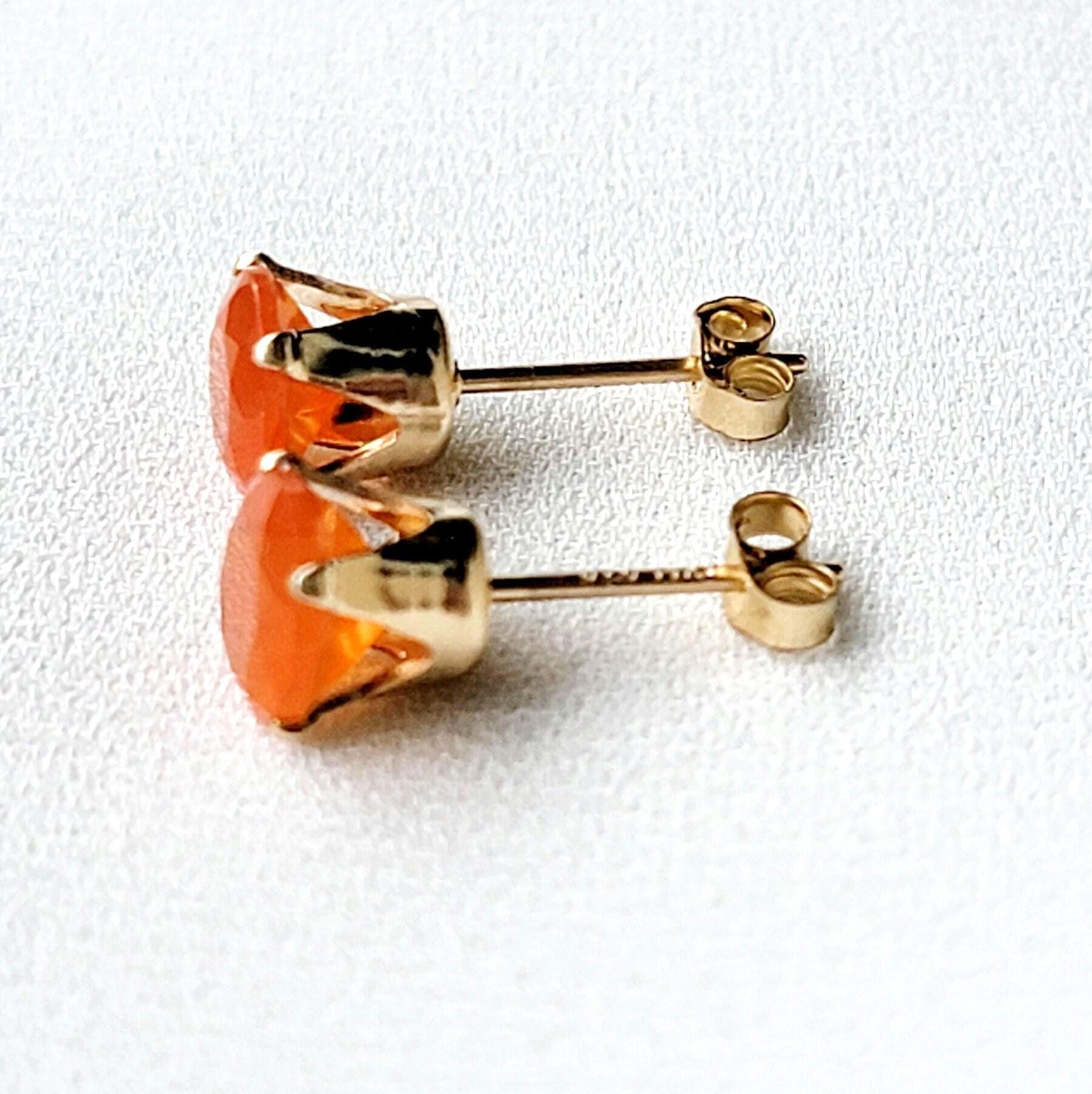 A pair of gold stud earrings with orange carnelian gemstones. The earrings have a simple design with a round gemstone set in a gold setting.