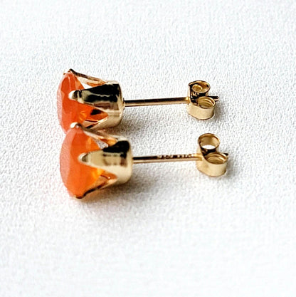 A pair of gold stud earrings with orange carnelian gemstones. The earrings have a simple design with a round gemstone set in a gold setting.