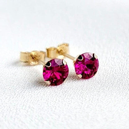 A pair of gold stud earrings with fascia colored ruby gemstones. The earrings are small and round, with a simple design.