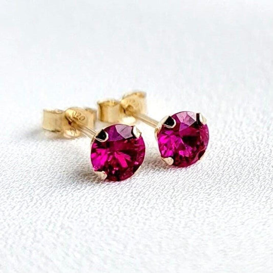 A pair of gold stud earrings with fascia colored ruby gemstones. The earrings are small and round, with a simple design.