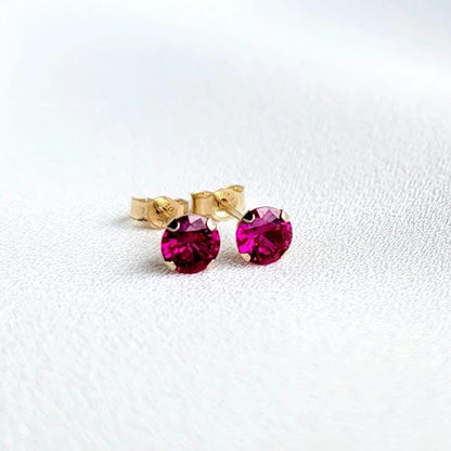 A pair of gold stud earrings with fascia colored ruby gemstones. The earrings are small and round, with a simple design.