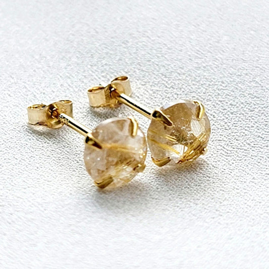 A pair of gold earrings with a clear quartz stone with gold inclusions. The inclusions look like gold spikes that are going through a clear crystal. The stones are round and have a faceted cut.