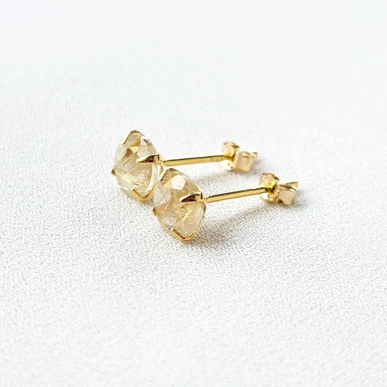 A pair of gold earrings with a clear quartz stone with gold inclusions. The inclusions look like gold spikes that are going through a clear crystal. The stones are round and have a faceted cut.