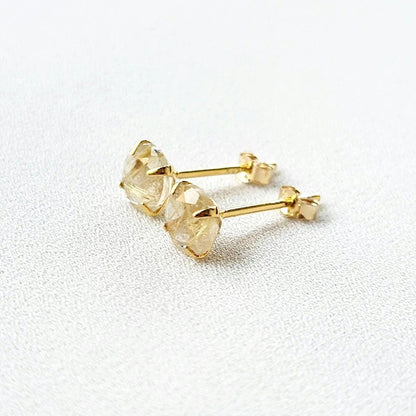 A pair of gold earrings with a clear quartz stone with gold inclusions. The inclusions look like gold spikes that are going through a clear crystal. The stones are round and have a faceted cut.