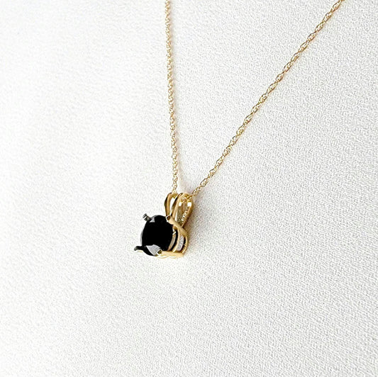 A gold chain necklace with a black gemstone pendant. The pendant is set in a gold setting with a black onyx gemstone.