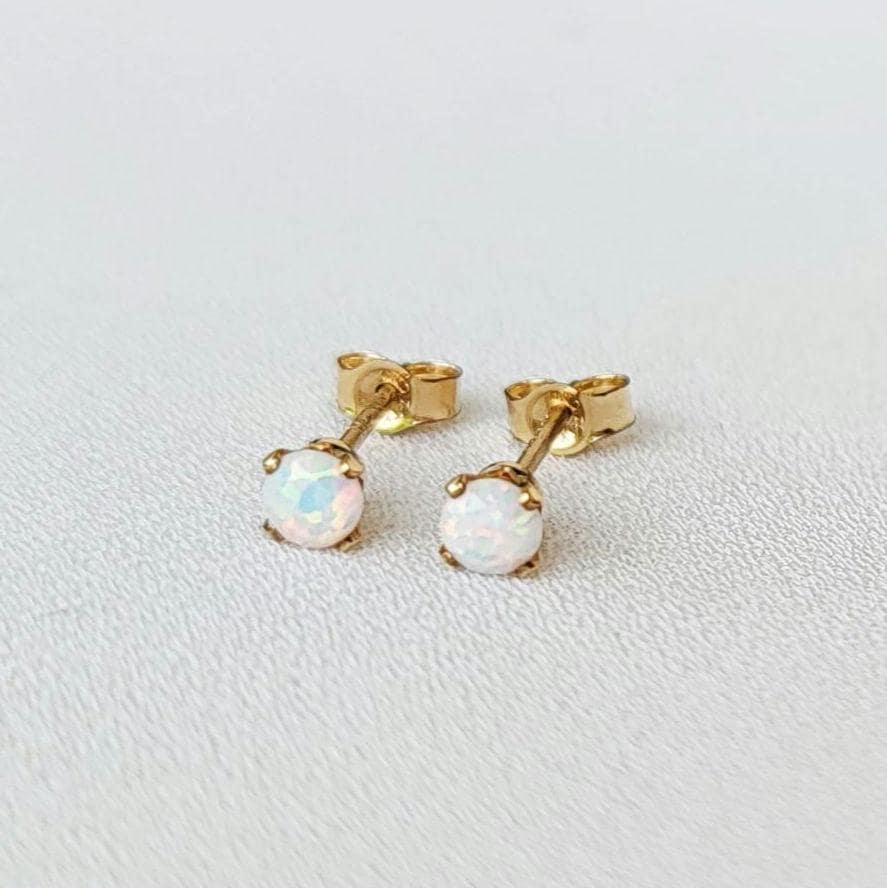 A pair of gold stud earrings with white opalite gemstones. The earrings are small and delicate, and the opalites have a subtle iridescent shimmer.