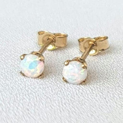 A pair of gold stud earrings with white opalite gemstones. The earrings are small and delicate, and the opalites have a subtle iridescent shimmer.