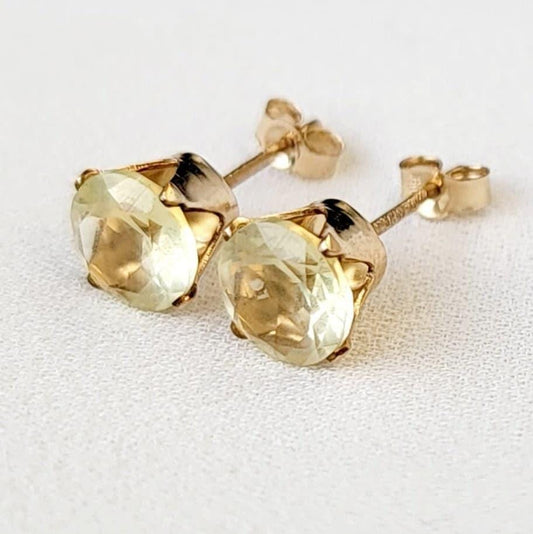 A pair of gold earrings with round shaped light yellow lemon quartz gemstones