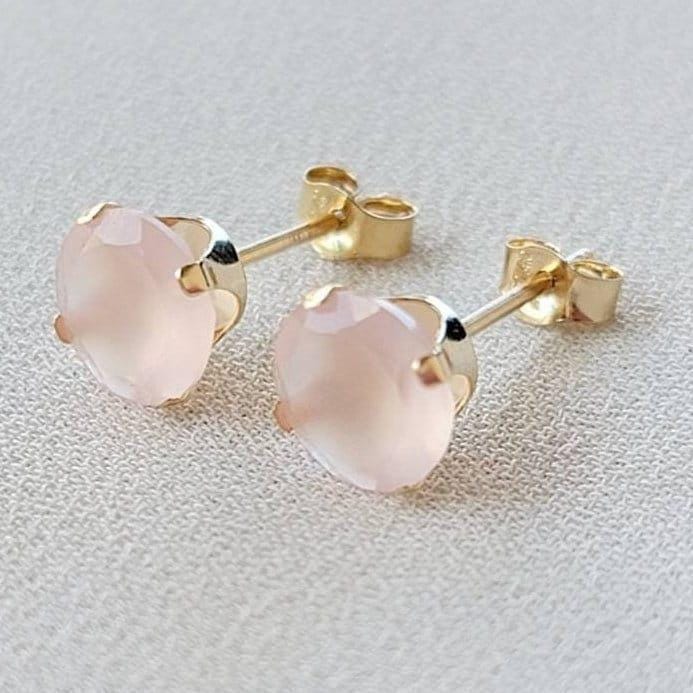 A pair of gold stud earrings with pink gemstone accents. The earrings are made of 14k gold and feature a round, faceted gemstone in a prong setting.