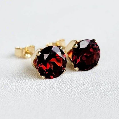 A pair of gold stud earrings with round red garnet gemstones.