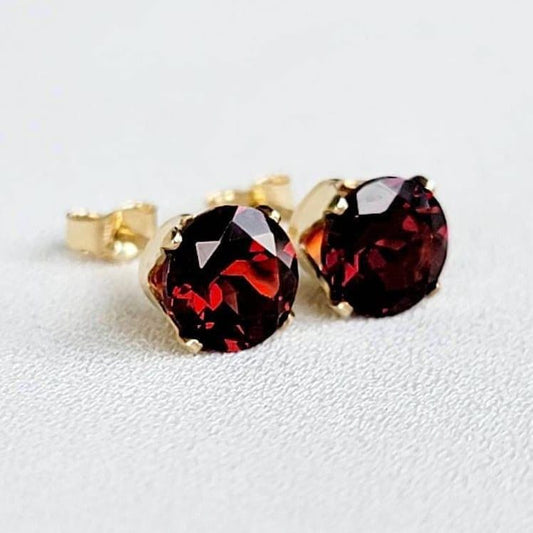 A pair of gold stud earrings with round red garnet gemstones.